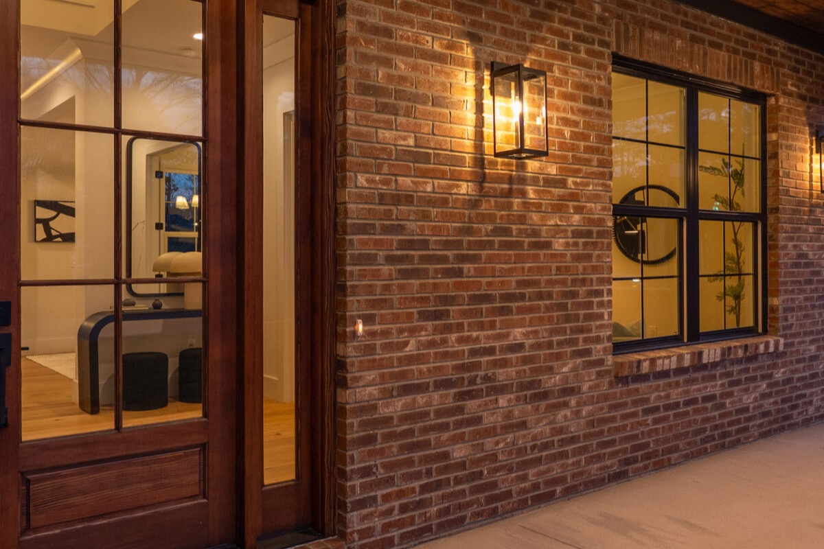 Covered brick entry porch with a wood ceiling, pendant sconces, and a glass-paneled front door