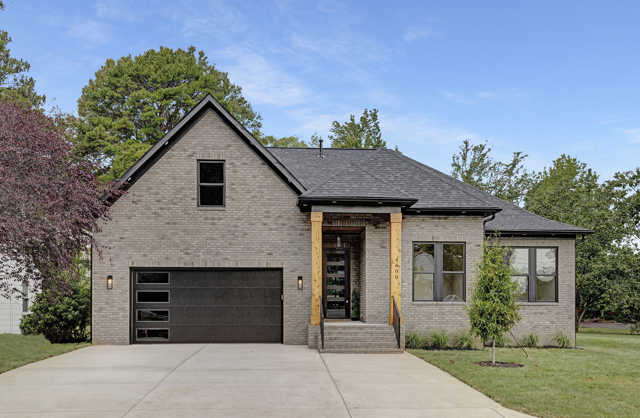 Light gray brick new construction home with wood-accented covered entry, photographed in daylight