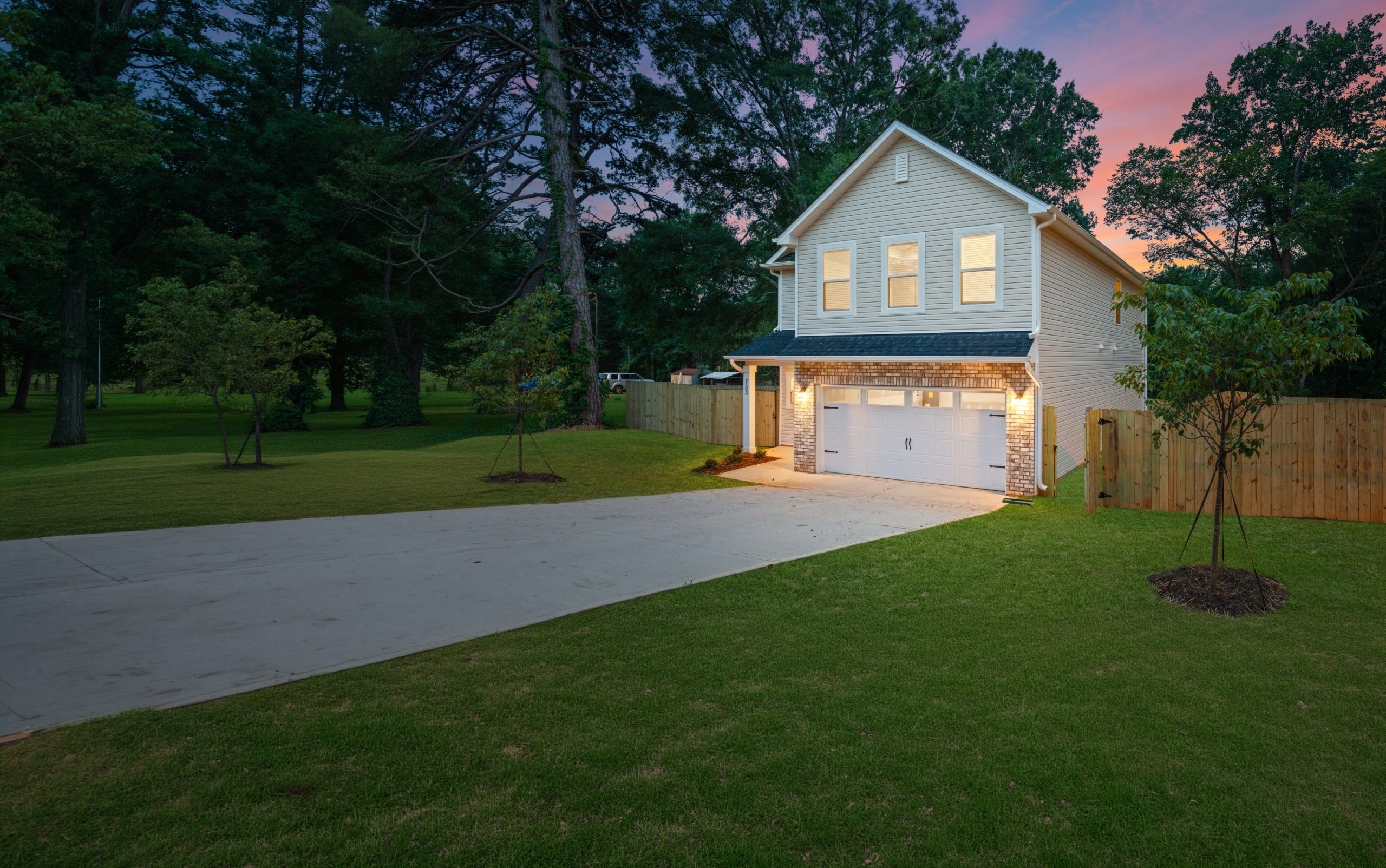 Two-story new construction home with cream siding and brick garage accents, photographed at dusk