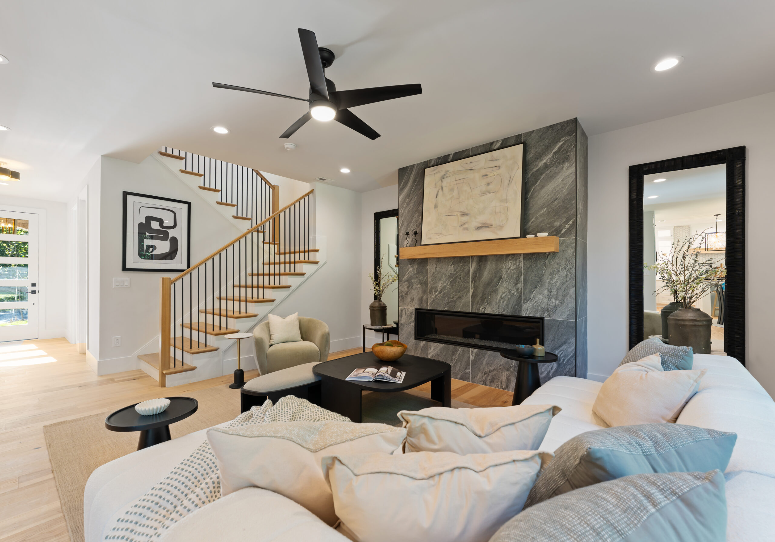 Open-concept living room with a black ceiling fan, curved staircase, and gray marble fireplace wall