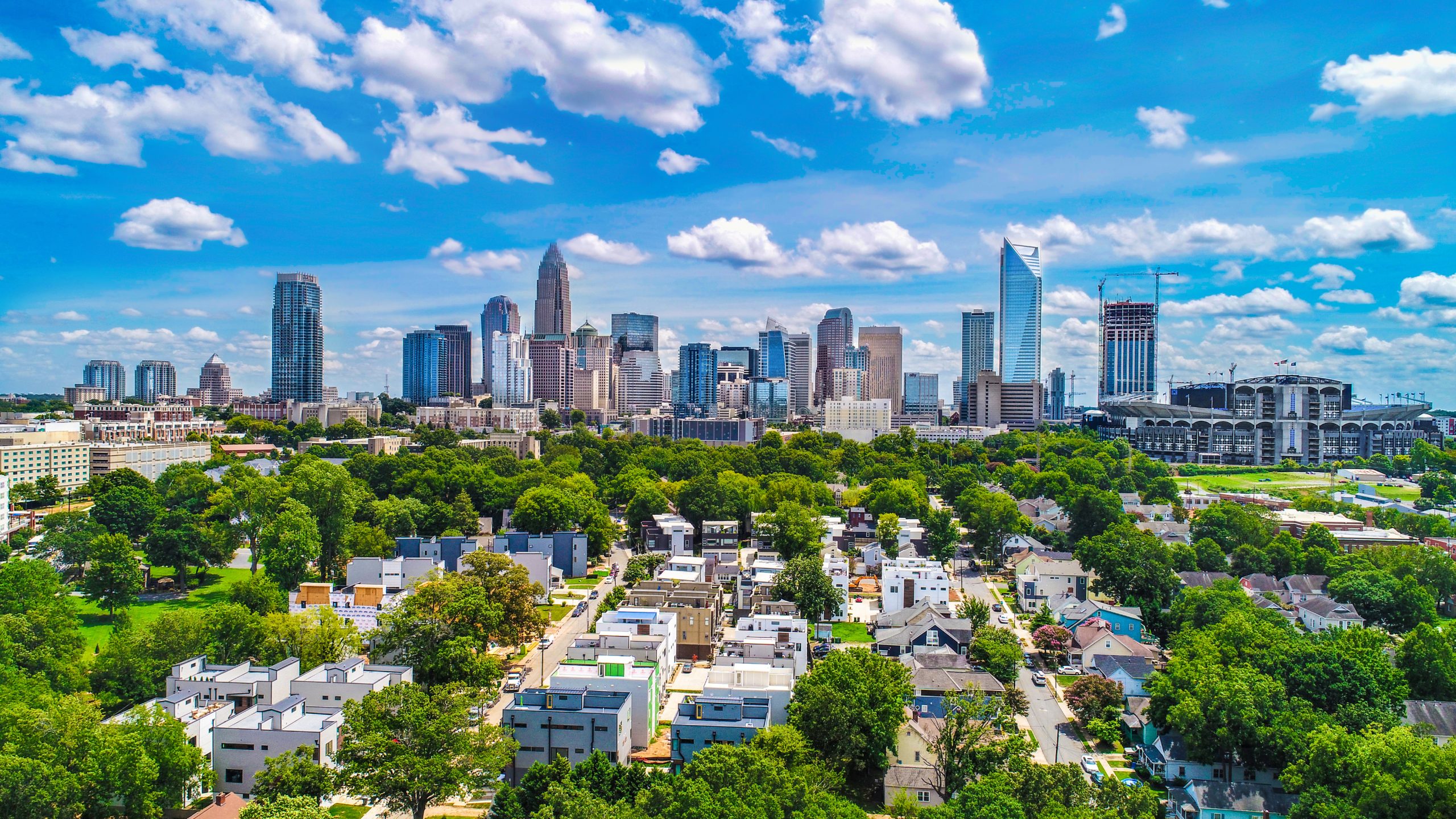 Aerial daytime view of the Charlotte, NC skyline beyond a tree-lined residential neighborhood