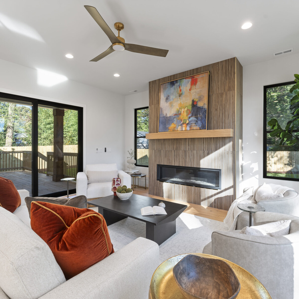 Open-concept living room with a linear gas fireplace set in a vertical wood surround, framed artwork above, and sliding doors to a covered porch